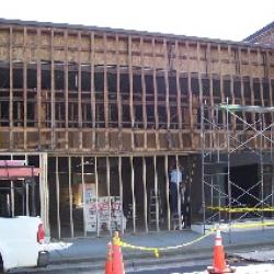 Workers remove the old glass storefront windows and install wall studs in preparation to give the building a traditional brick front facade. 